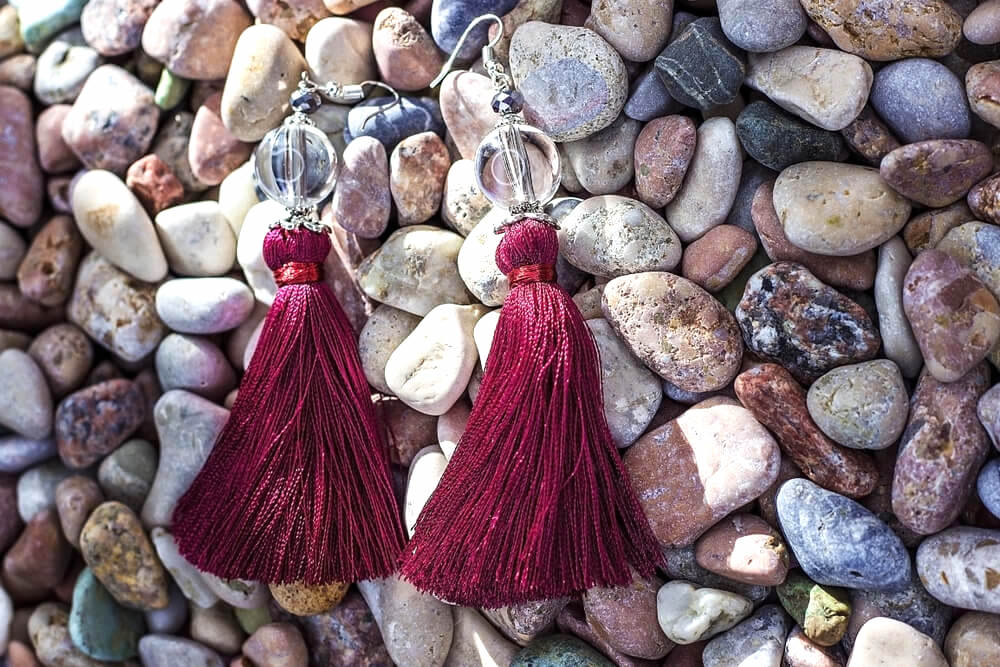 Berry-colored tassel earrings on beach pebbles