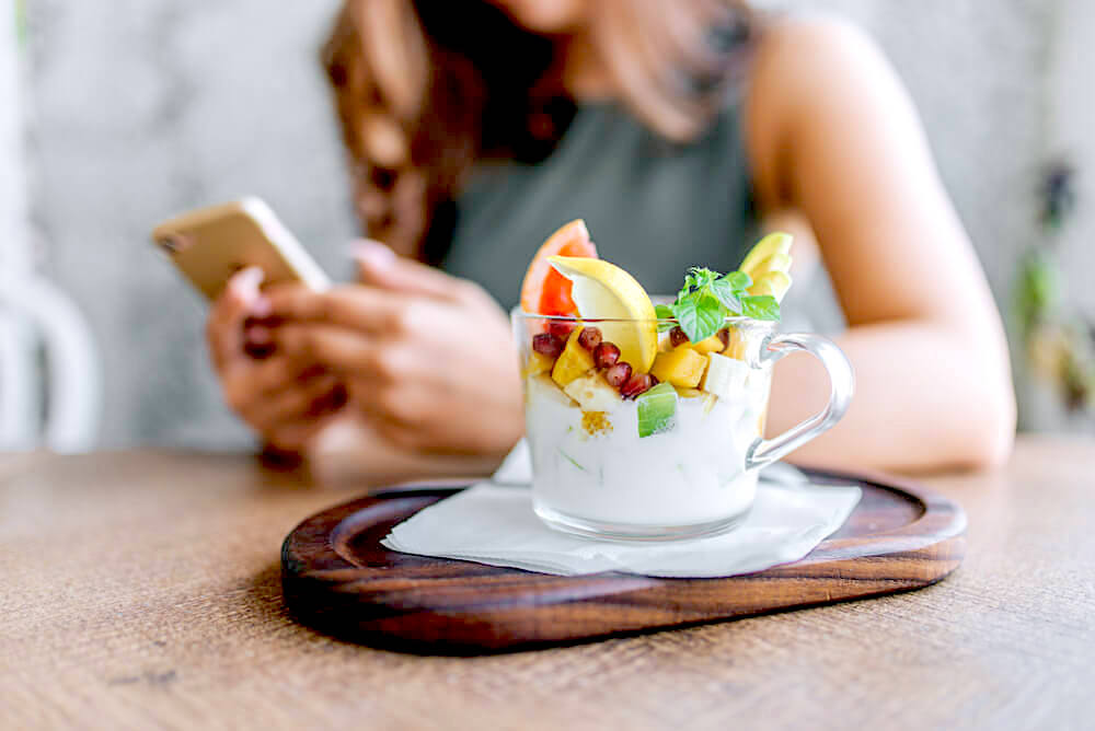 Bowl of yogurt with fruits, unknown woman on her phone