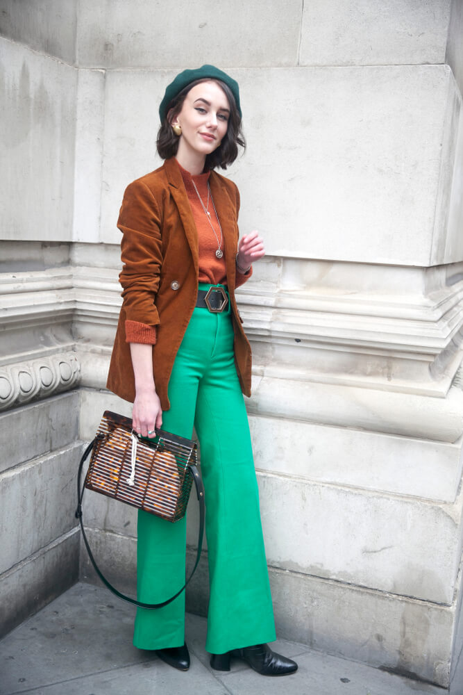 LONDON - FEBRUARY 15, 2019: Stylish attendees gathering outside 180 The Strand for London Fashion Week. Girl in green flared trousers and a brown jacket 