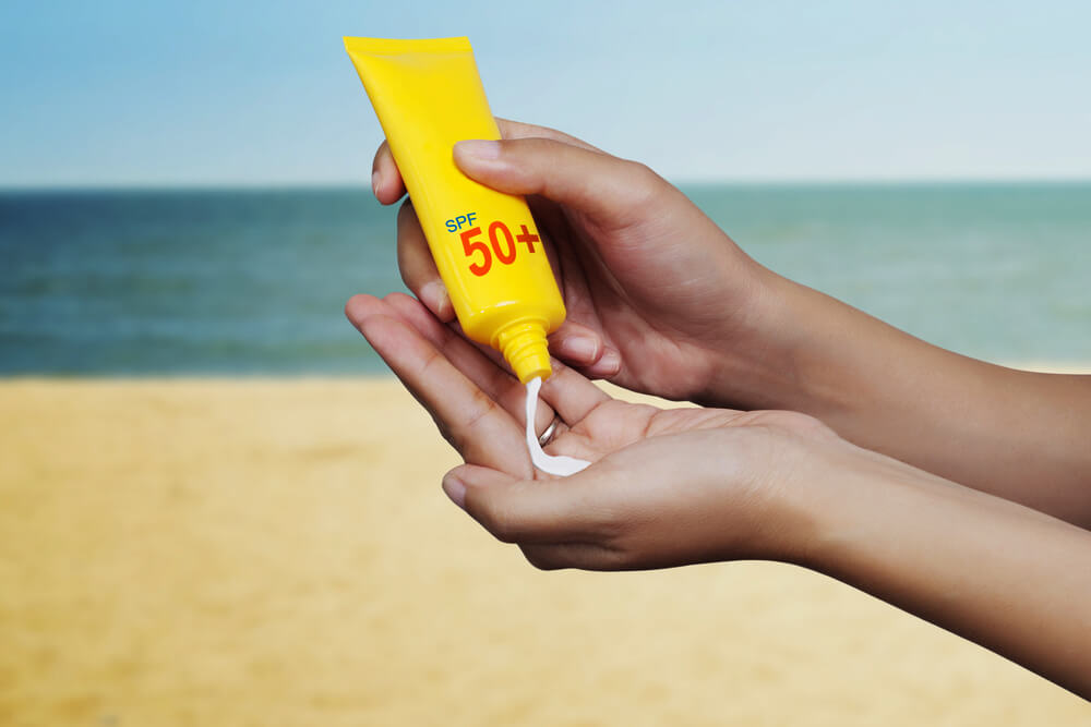 Squeezing sunscreen onto hands with beach and sea in background