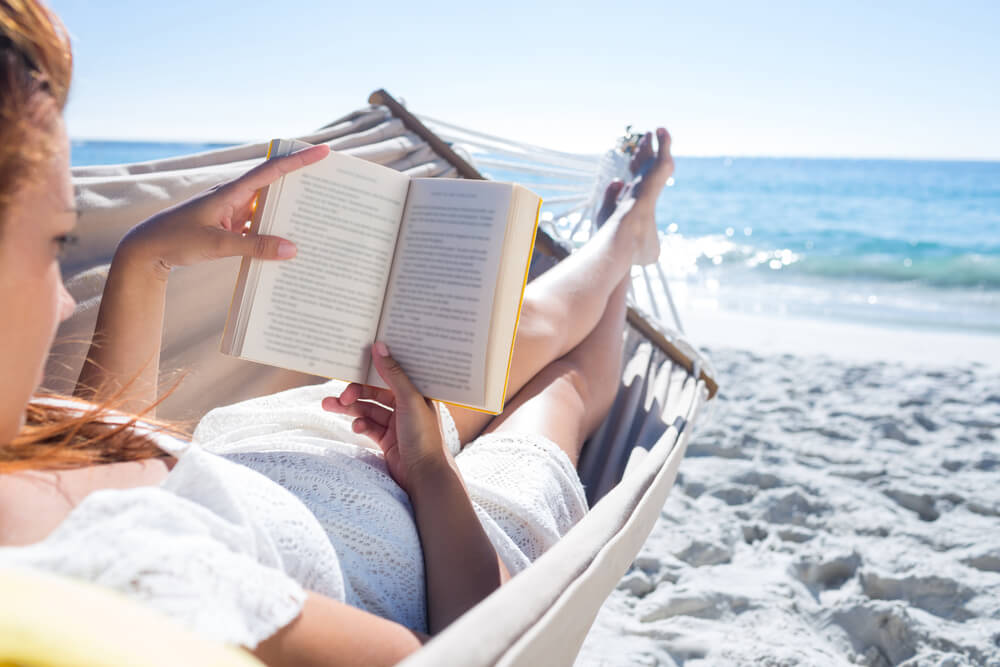 Woman reading book on hammock on beach