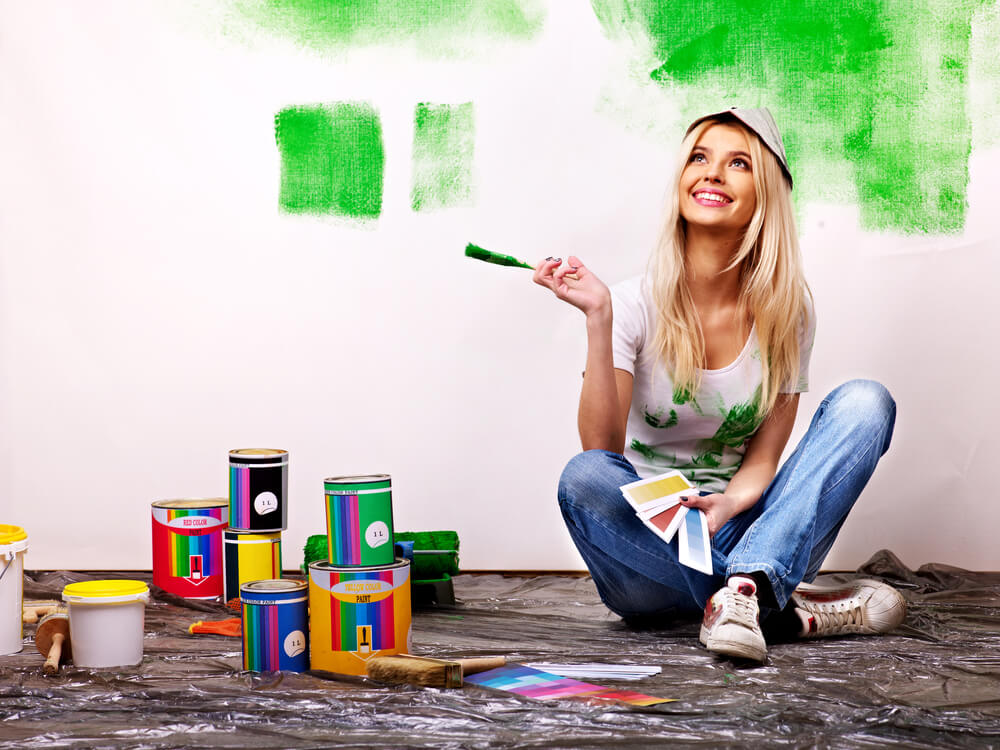 Woman holding paintbrush painting wall green